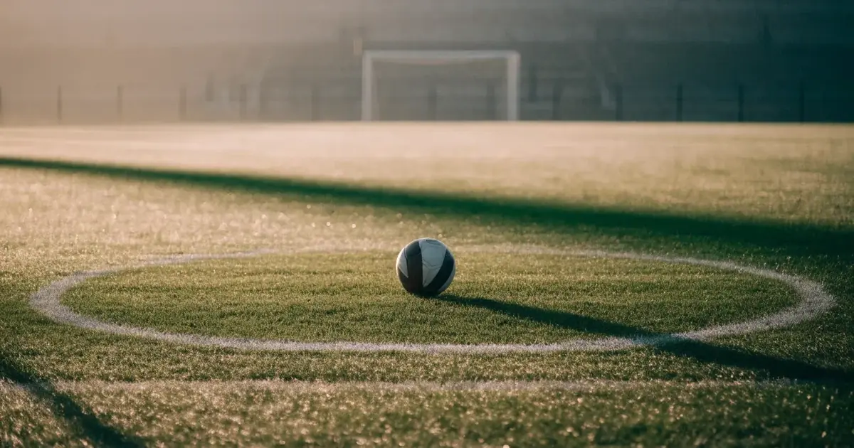 Uma bola de futebol no ponto central de um relvado, à luz da manhã